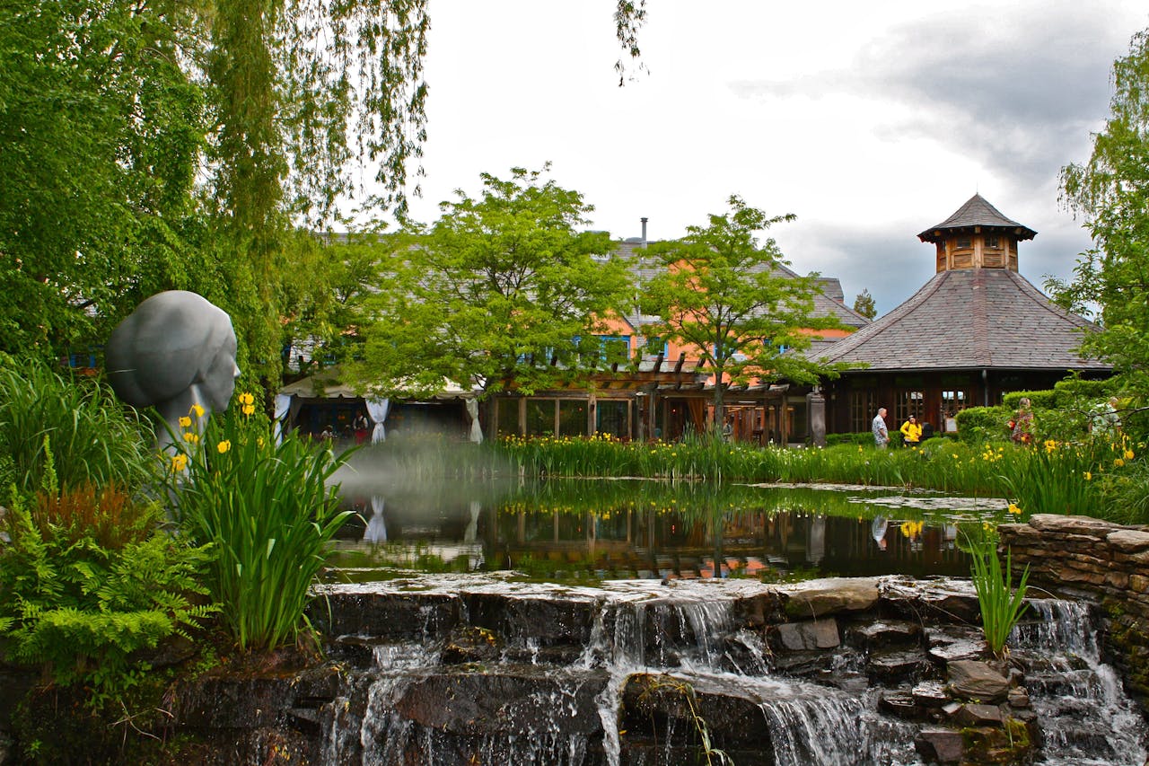trusted-partner Scenic garden with a pond, waterfall, and sculpture under a cloudy sky.